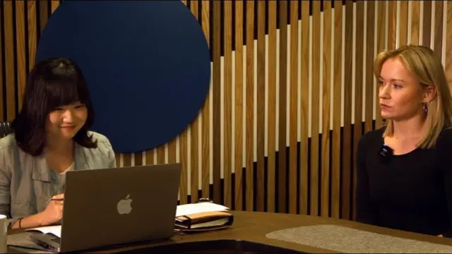 Una mujer sonríe frente a un computador portátil: está hablando con alguien por videollamada. Otra mujer la mira.