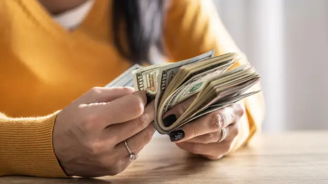 Primer plano de las manos de una mujer contando billetes de 100 dólares